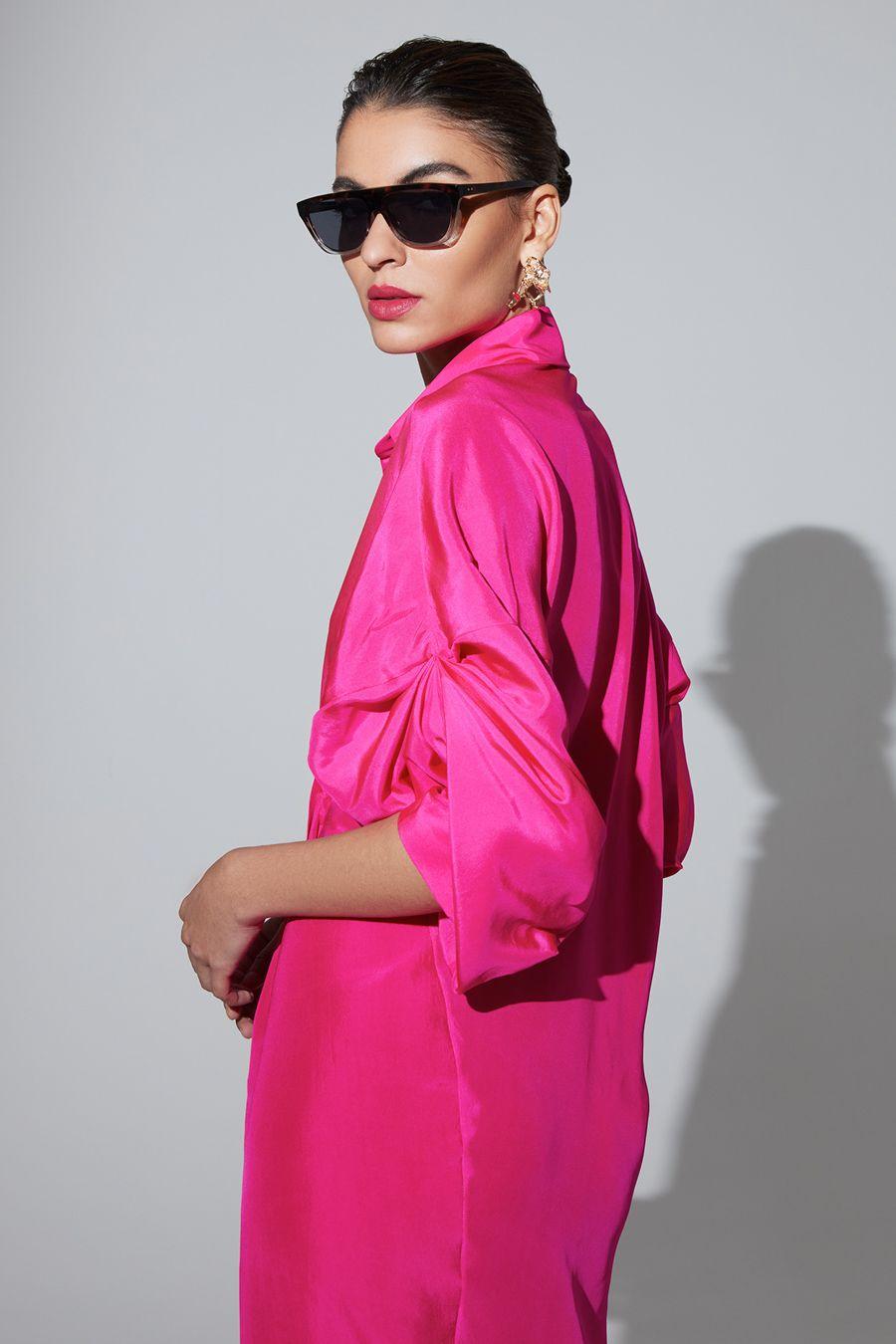 Woman wearing a bright pink outfit with sunglasses against a plain background