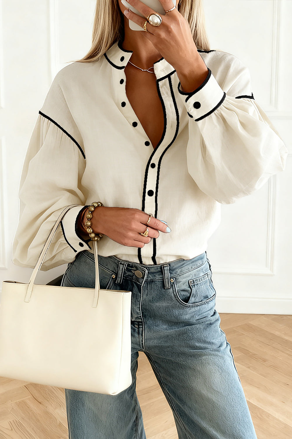 Person wearing a white blouse with black trim and blue jeans, holding a beige handbag.