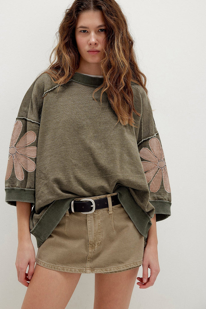 Woman wearing a green oversized sweatshirt with floral sleeves and a beige skirt on a white background