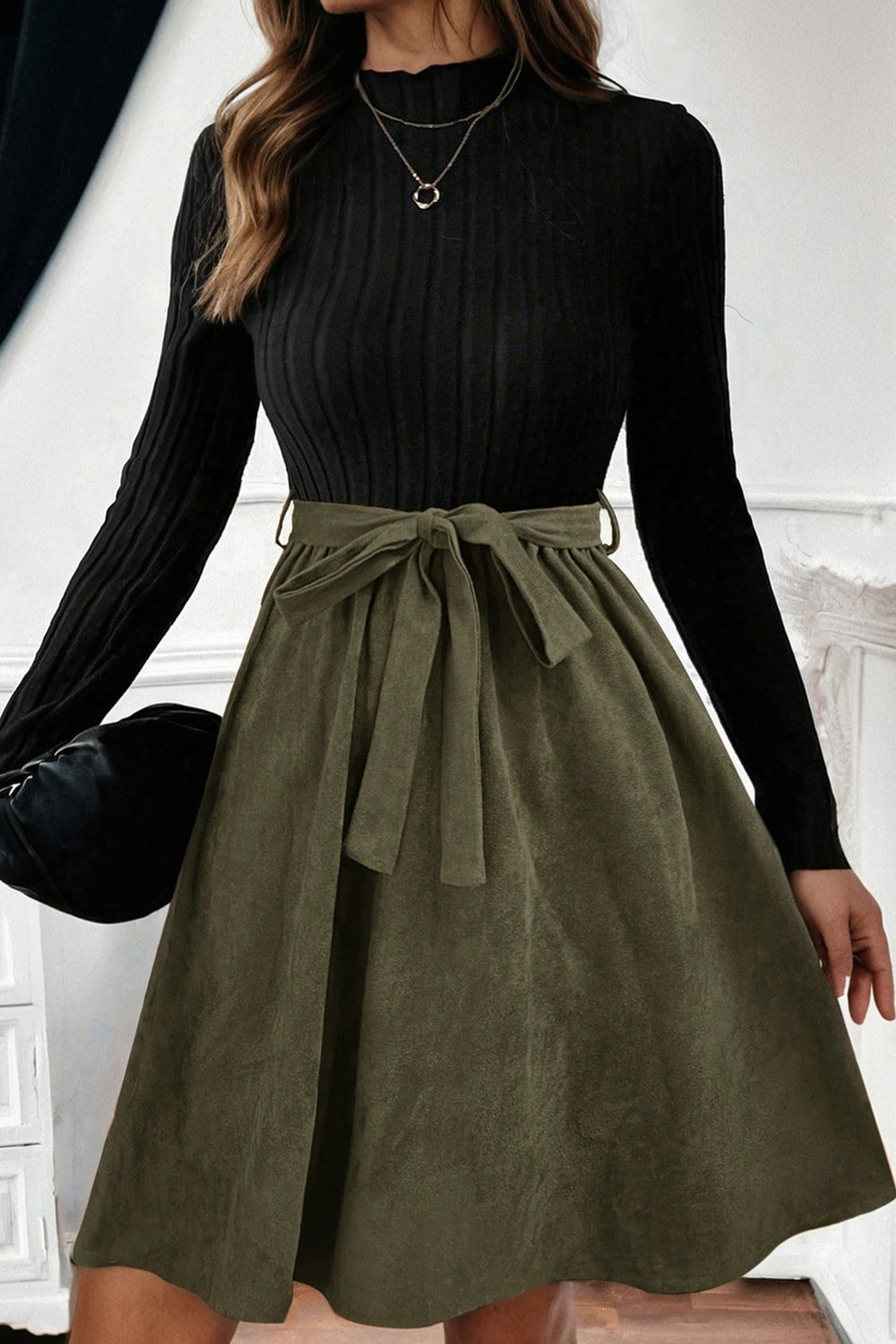 Person wearing a black long-sleeve top and olive green skirt with a belt.