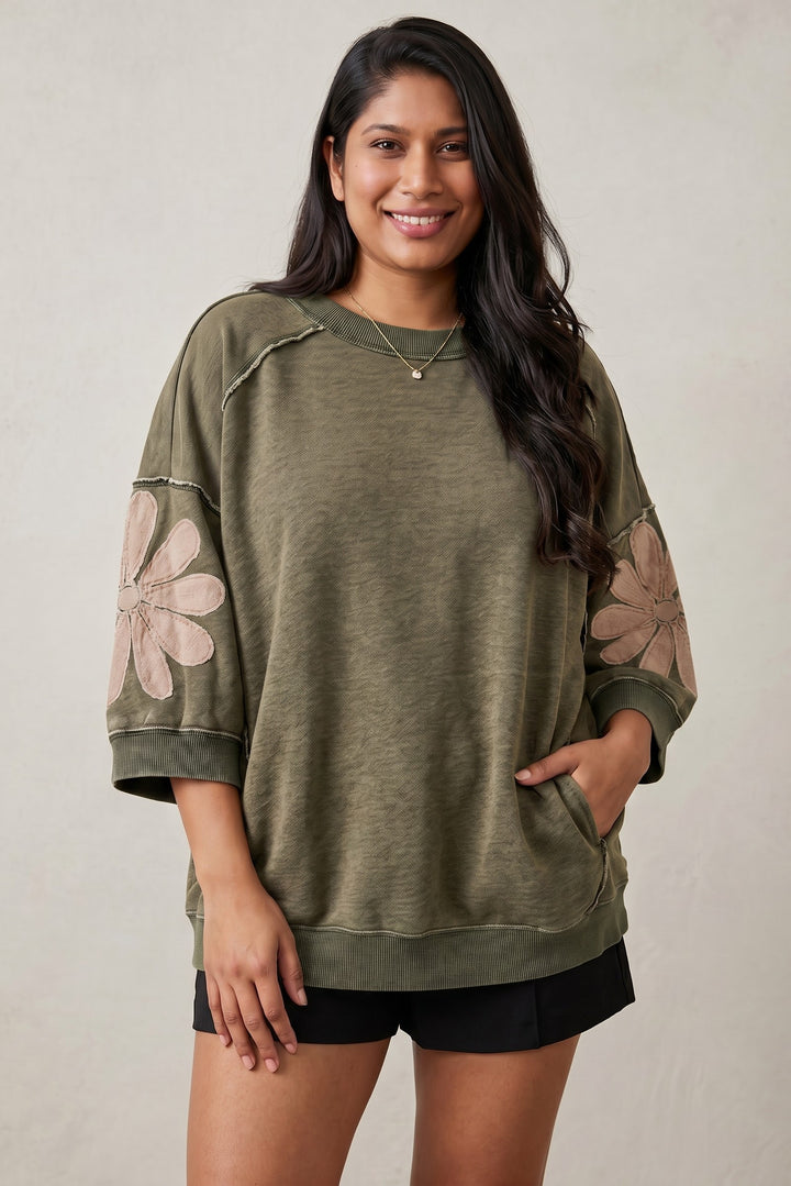 Errabelly olive green mineral wash oversized top with 3/4 sleeves, raw seams, and patchwork flower details on sleeves. Features a crew neck and front pocket.