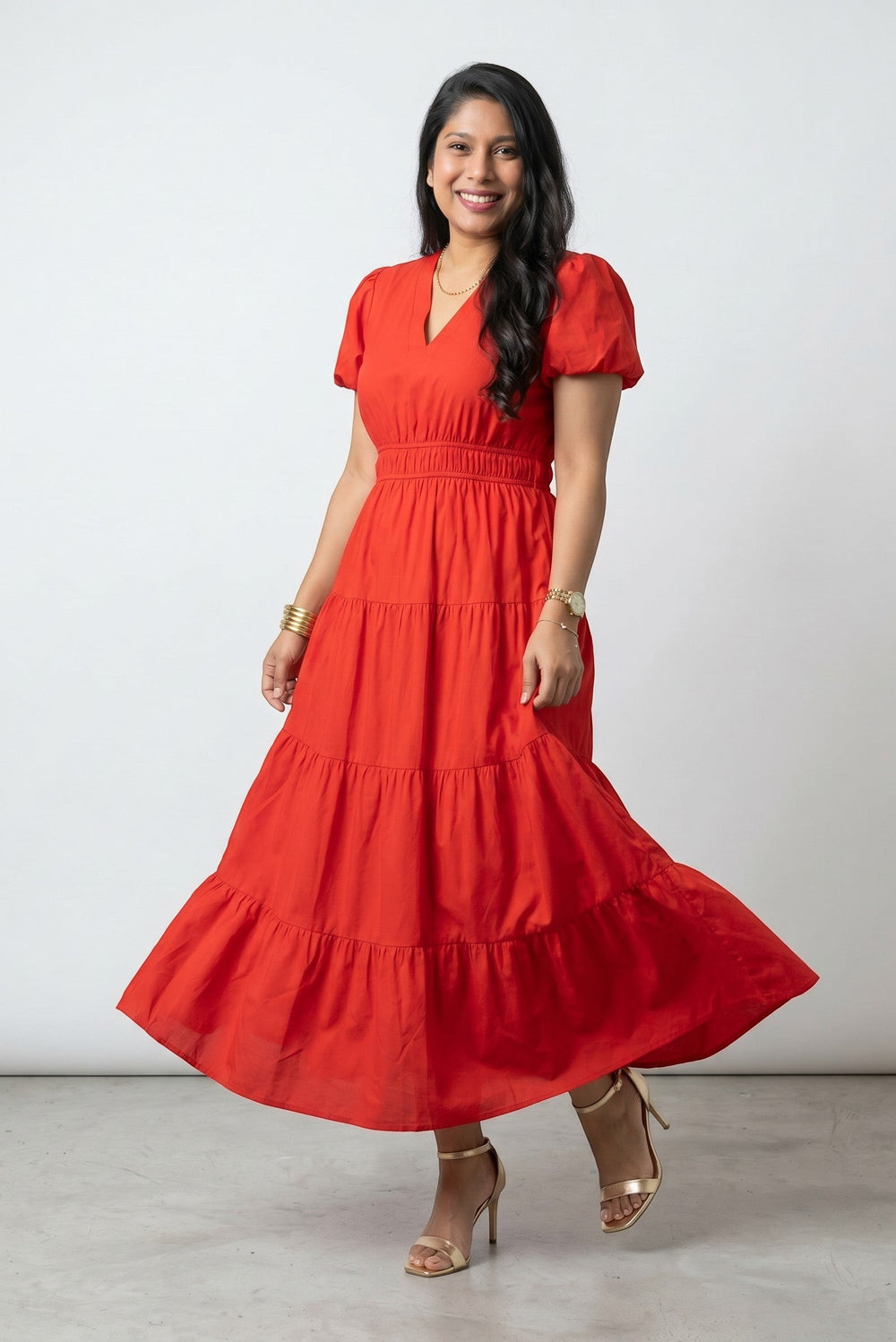 Errabelly coral red tiered maxi dress with V neck, short puff sleeves, and high waist. Model wears gold jewelry.