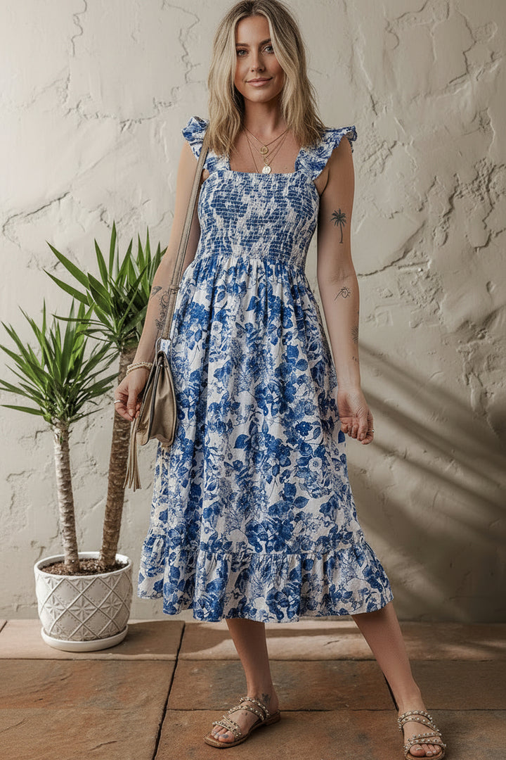 Woman wearing a blue floral dress standing indoors with a plant in the background